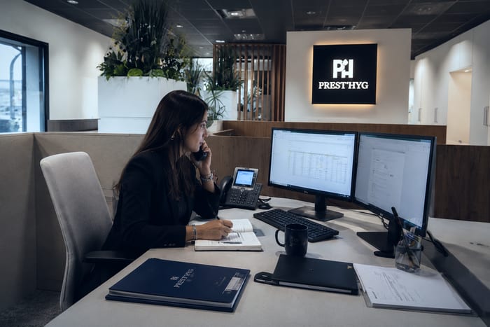 Une collaboratrice du service ADV au téléphone à son poste, devant l’enseigne lumineuse Prest'Hyg de l’accueil.